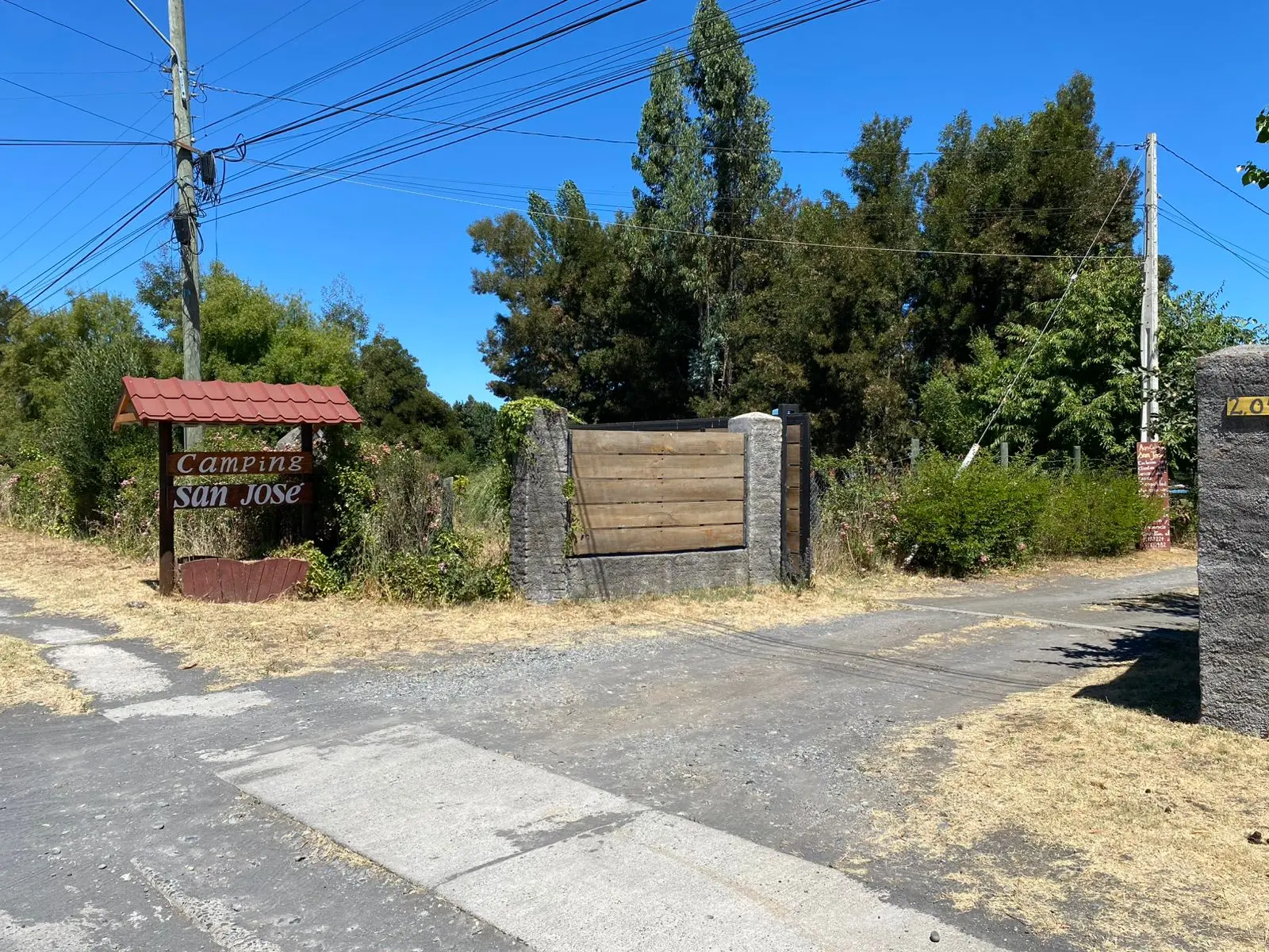 Pasarela de madera sobre el río Laja con sauces llorones y cielo azul en Camping San José